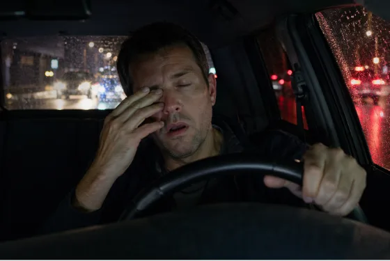 Drowsy driver rubbing his eyes behind the wheel